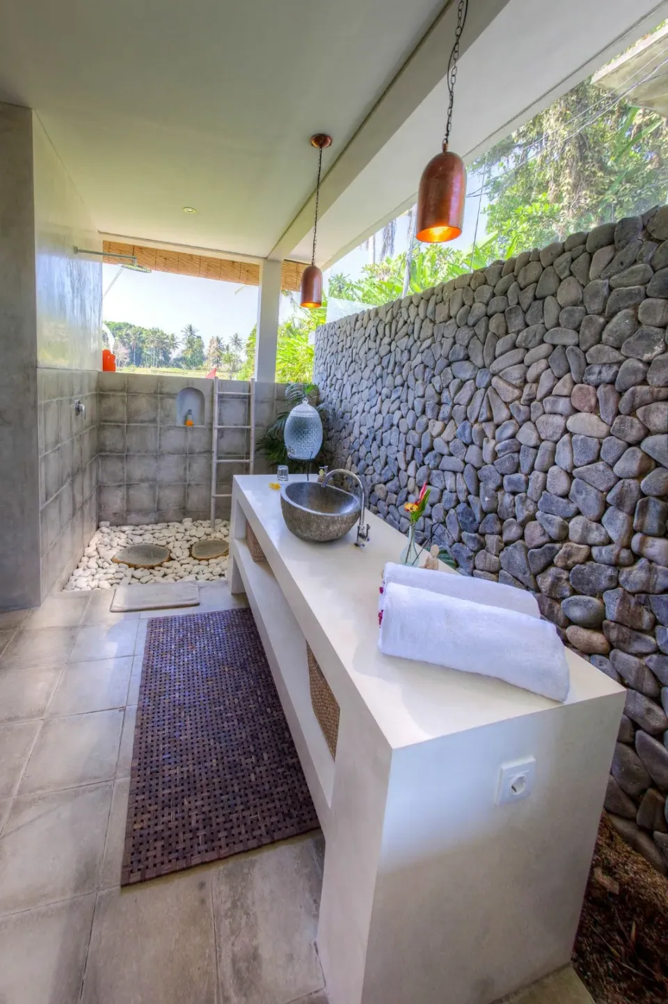A long washbasin in an open-air stone-walled bathroom