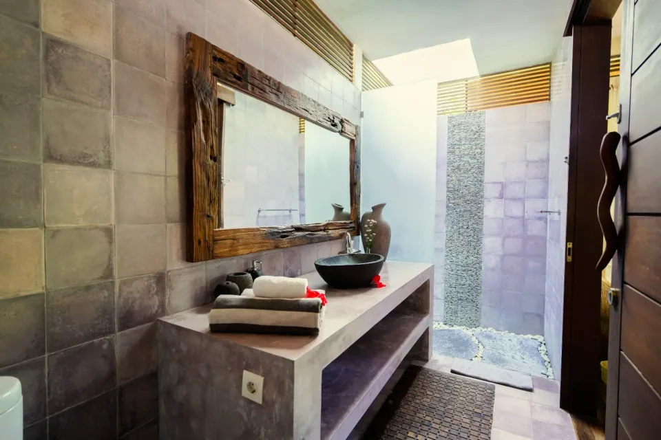A stone washbasin and mirror beside a tiled shower