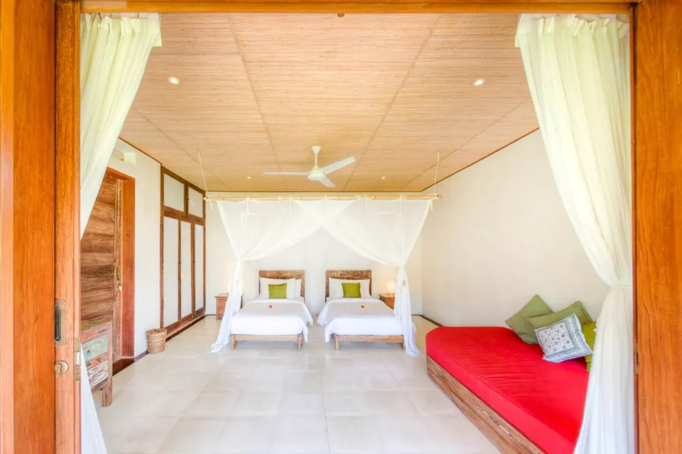Twin canopy beds and a red daybed beneath a timber ceiling